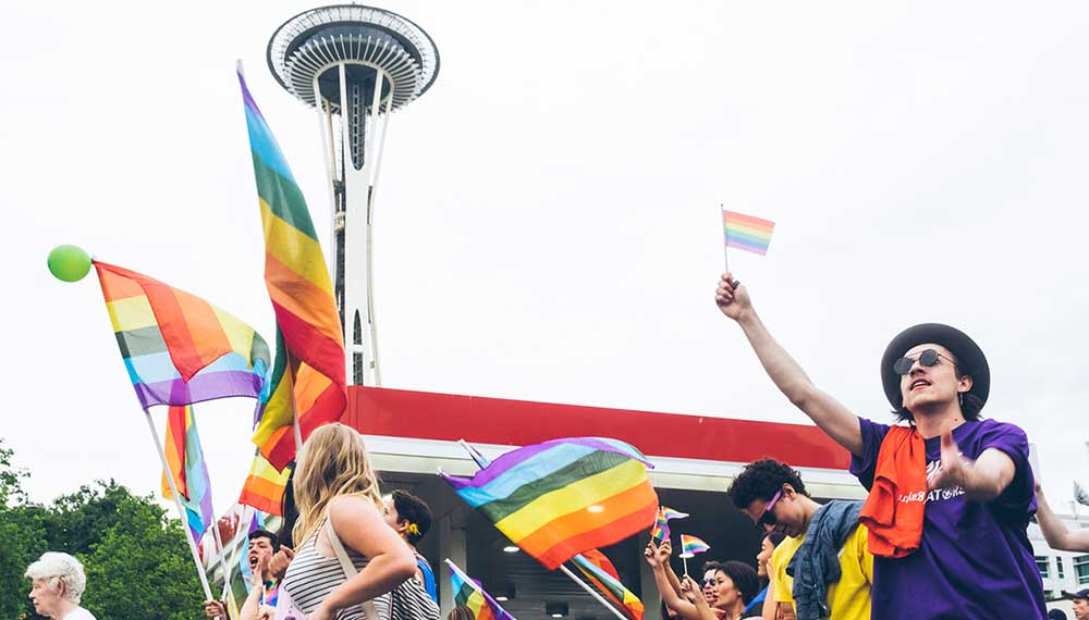 people carryihng a pride flags in front of space needle